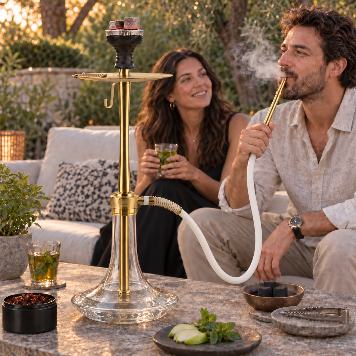 Oduman Cosmo clear glass and gold shisha pipe in a garden setting with adults, flavour, charcoal and tongs.