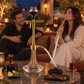Oduman Cosmo clear glass and gold shisha pipe in a lounge setting with adults, flavour, charcoal and tongs.