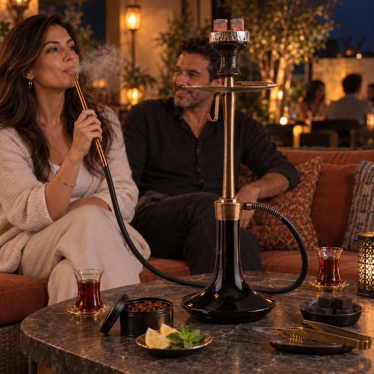 Black-glass and bronze Oduman Cosmo shisha pipe in a lounge setting with adults and shisha accessories.
